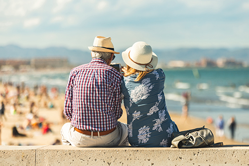 Older couple sitting at the seaside enjoying the view of happy families and bright sunshine